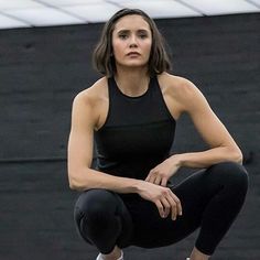 a woman squatting on the ground with her hands behind her back and looking up