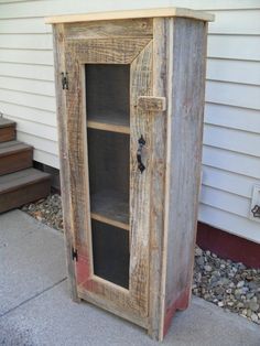 an old wooden cabinet sitting on the side of a house next to some rocks and gravel