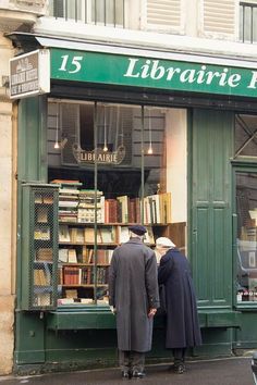 two men are standing in front of a book store looking at books on the shelves