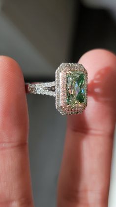a close up of a person's hand holding a ring with a green diamond