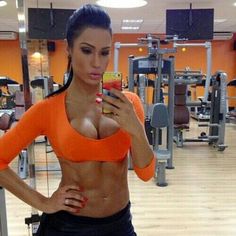 a woman taking a selfie in the gym with her cell phone while wearing an orange crop top