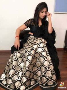 a woman is sitting on the floor in a black and gold dress with her hands to her face