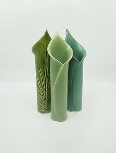 three green vases sitting side by side on a white surface