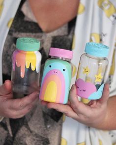 a woman holding three jars with different designs on them and one has a rainbow design