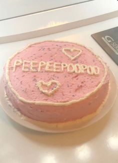 a pink cake with the word peepobo on it sitting on a table next to a laptop