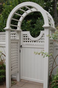 a white gate with an arch and lattice design on the top is surrounded by shrubbery