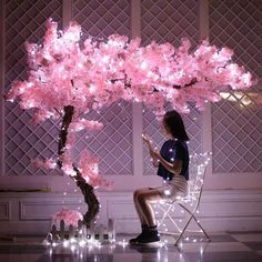 a woman sitting in a chair under a pink tree