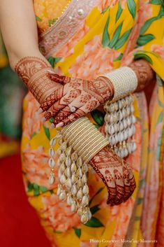 a woman in yellow and orange sari holding her hands with henna on it