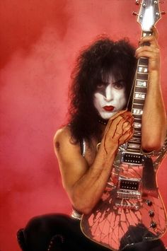 a man with white makeup and black hair holding an electric guitar in front of his face