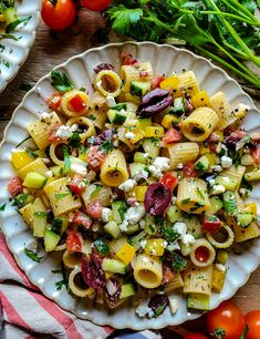 a white plate topped with pasta salad next to tomatoes