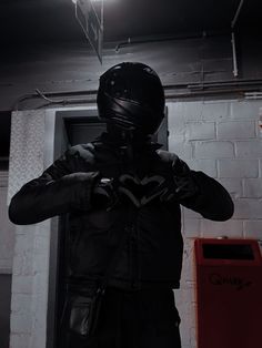 a man in a black jacket and helmet standing next to a wall with a light on it