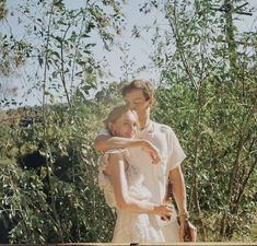 a man and woman standing next to each other in front of some trees with their arms around each other