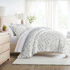 a bed with white and gray comforter in a bedroom next to a lamp on a dresser