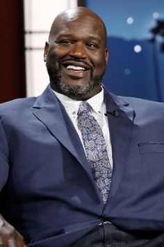 a bald man in a blue suit and tie smiles at the camera while sitting down