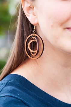 a woman wearing large wooden earrings with an oval design on the front and back of her ear