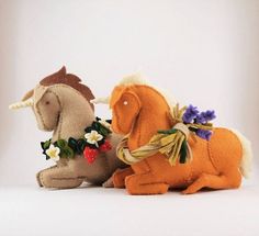 two stuffed unicorns sitting next to each other on a white surface with flowers in their hair