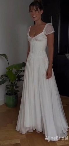 a woman in a white dress standing on a wooden floor next to a potted plant