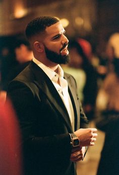 a man in a black suit and white shirt is looking off to the side with his hand on his hip