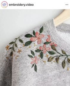 a gray sweater with pink flowers on it and green leaves embroidered on the chest, along with a wooden hanger