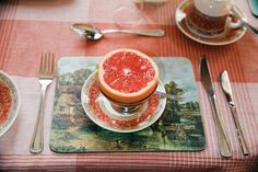 a grapefruit cut in half on a plate with silverware and utensils