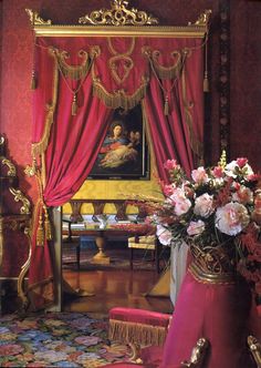 an ornately decorated room with red drapes and pink flowers in the centerpiece