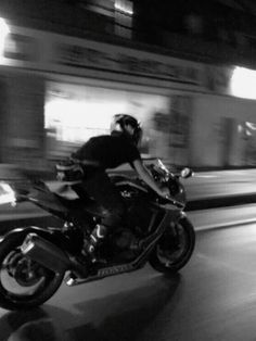 black and white photograph of a person riding a motorcycle on the road at night time
