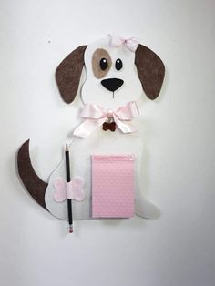 a paper dog with a pink notepad and pencil in it's mouth, sitting on top of a white wall