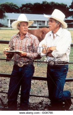 two men in cowboy hats standing next to a fence holding plates with food on them