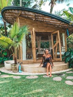 a woman sitting on top of a wooden bench in front of a gazebo surrounded by palm trees