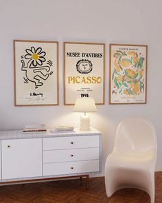 a white chair sitting next to a table with a lamp on top of it in front of two posters