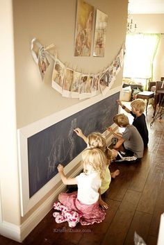 three children writing on a blackboard in front of a wall with pictures hanging above it