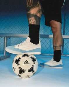 a man standing next to a soccer ball on top of a blue floor with his legs crossed