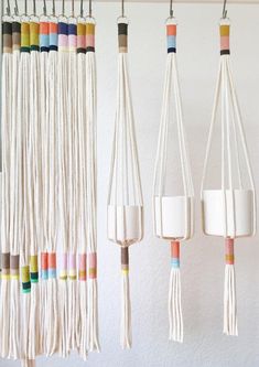 three macrame hangings with different colored cords and cups on them in front of a white wall