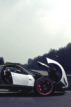 a white and black sports car driving down the road with its doors open on it's side