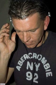 a man with headphones on his ears looking down at his cell phone while wearing a t - shirt that says abercumb ny