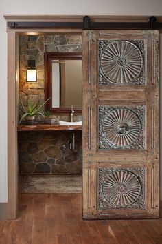 an open door leading to a bathroom with stone walls and wood flooring, along with a mirror on the wall