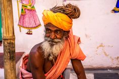 an old man with a yellow turban sits on the ground next to a pole