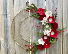 a christmas wreath with red and white flowers on a wooden fence next to a wine glass