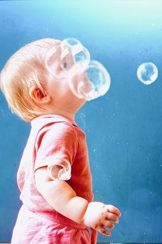 a toddler looking up at soap bubbles floating in the air over her head and body