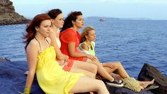 four women sitting on rocks in front of the ocean