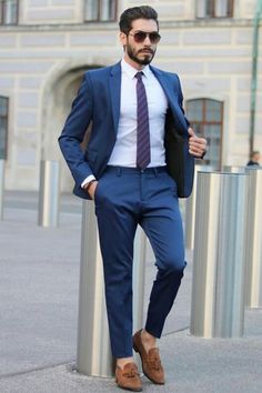 a man in a blue suit and tie standing next to a metal pole with his hands in his pockets