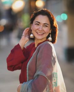 a smiling woman with her hand on her head, wearing a red shirt and carrying a white bag