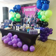 a table topped with lots of purple and green balloons next to a fortnite sign
