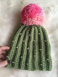 a hand holding a green and pink knitted beanie with pom - pom
