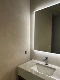 a bathroom sink under a large mirror with lights on the wall and below it is a white counter top