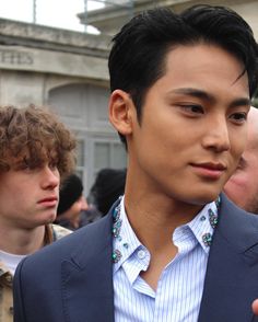 a man in a blue suit and white shirt is looking at his cell phone while other people are standing around him