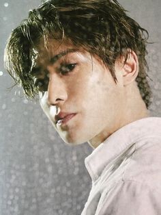 a young man with wet hair standing in front of a rain soaked wall and looking at the camera
