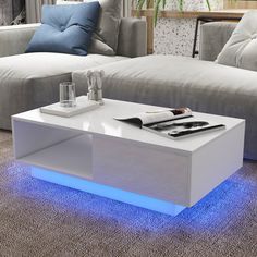 a white coffee table with blue lights on it in front of couches and pillows