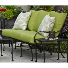 a green couch with pillows on it sitting in front of some flowers and potted plants