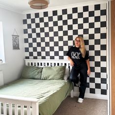 a woman standing in front of a black and white checkered wall next to a bed